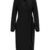 A professional woman wearing a sophisticated black long-sleeve coat dress, featuring an elegant tie-waist belt and notched lapels, styled over a white shirt for a polished executive business look.