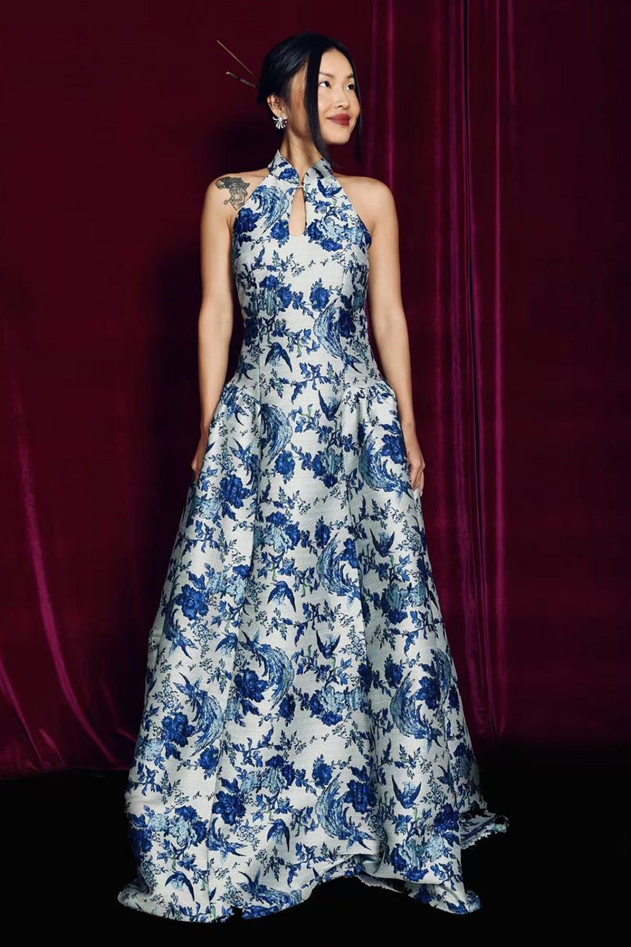 A stunning modern oriental gala dress featuring a classic blue and white porcelain floral print, an elegant halter neck with keyhole detail, and a voluminous A-line full skirt for a sophisticated formal look.