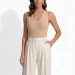 A professional woman modeling a sleeveless chocolate brown top and cream wide-leg pleated trousers, styled with a patterned yellow silk scarf and bold gold jewelry for a sophisticated office aesthetic.