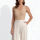 A professional woman modeling a sleeveless chocolate brown top and cream wide-leg pleated trousers, styled with a patterned yellow silk scarf and bold gold jewelry for a sophisticated office aesthetic.