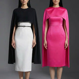Two professional women wearing sophisticated cape-style dresses: one in a classic black and white monochrome with a thin belt, and the other in a vibrant magenta pink, perfect for a powerful and elegant evening look.