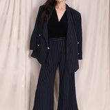 A professional woman wearing sophisticated navy blue pinstripe wide-leg trousers, featuring a high-waisted tailored fit and elegant vertical stripes for a polished executive office look.
