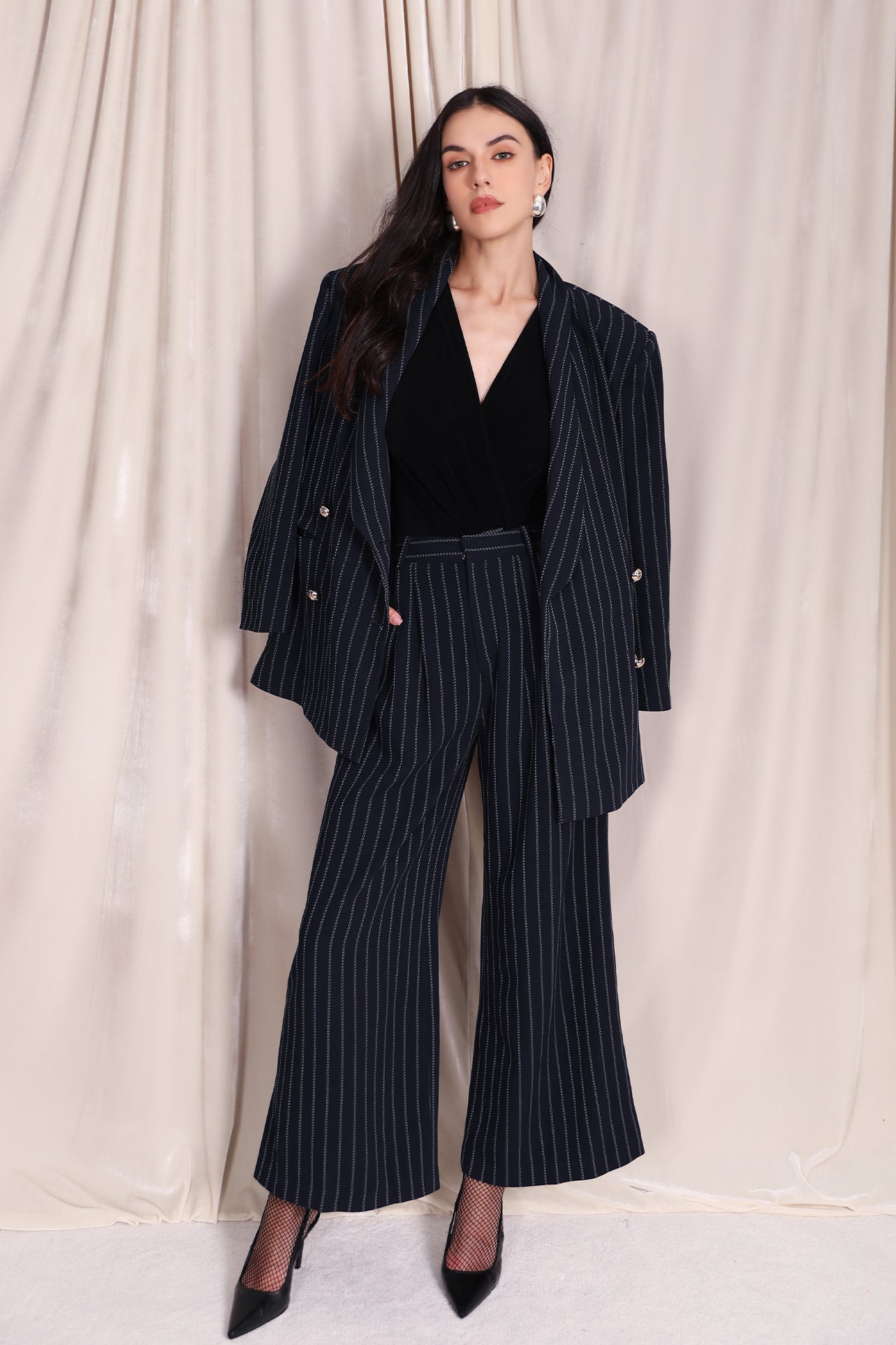 A professional woman wearing sophisticated navy blue pinstripe wide-leg trousers, featuring a high-waisted tailored fit and elegant vertical stripes for a polished executive office look.