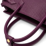 A sophisticated plum purple tote bag crafted from premium pebbled leather, displayed next to a matching shade of luxury lipstick, representing an elegant executive fashion set.