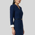 A professional woman wearing a sophisticated navy blue V-neck sheath dress, featuring elegant white contrast turn-up cuffs and a slim black belt with a gold buckle for a polished executive look.
