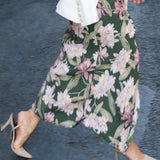 A professional woman wearing a sophisticated dark green wrap dress with a vibrant pink floral print, featuring long sleeves and a slimming waist-tie for an elegant spring look.