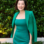 A professional woman wearing a sophisticated emerald green sleeveless dress, featuring a classic square neckline and a flattering tailored sheath silhouette for an elegant executive look.