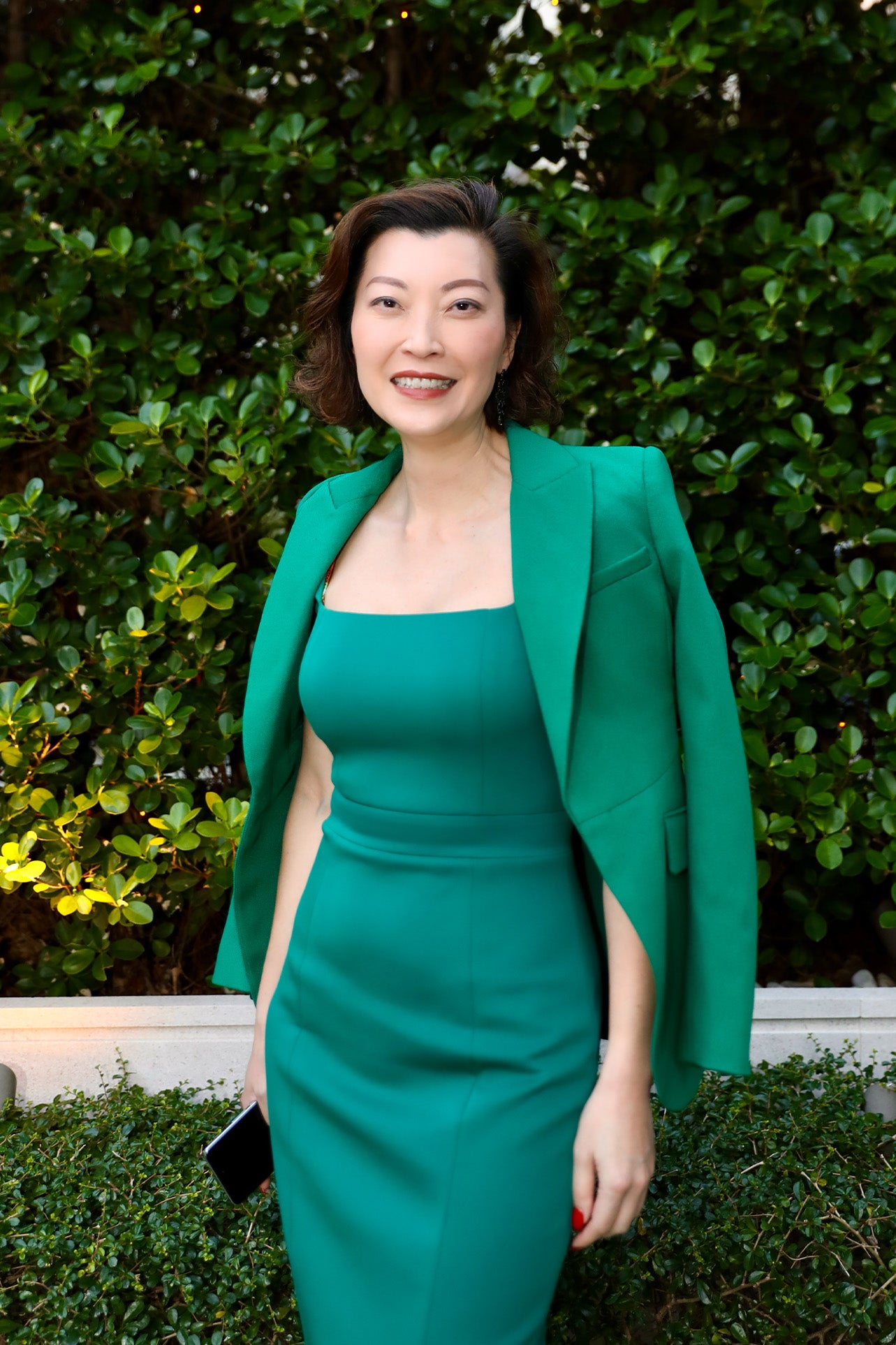 A professional woman wearing a sophisticated emerald green sleeveless dress, featuring a classic square neckline and a flattering tailored sheath silhouette for an elegant executive look.