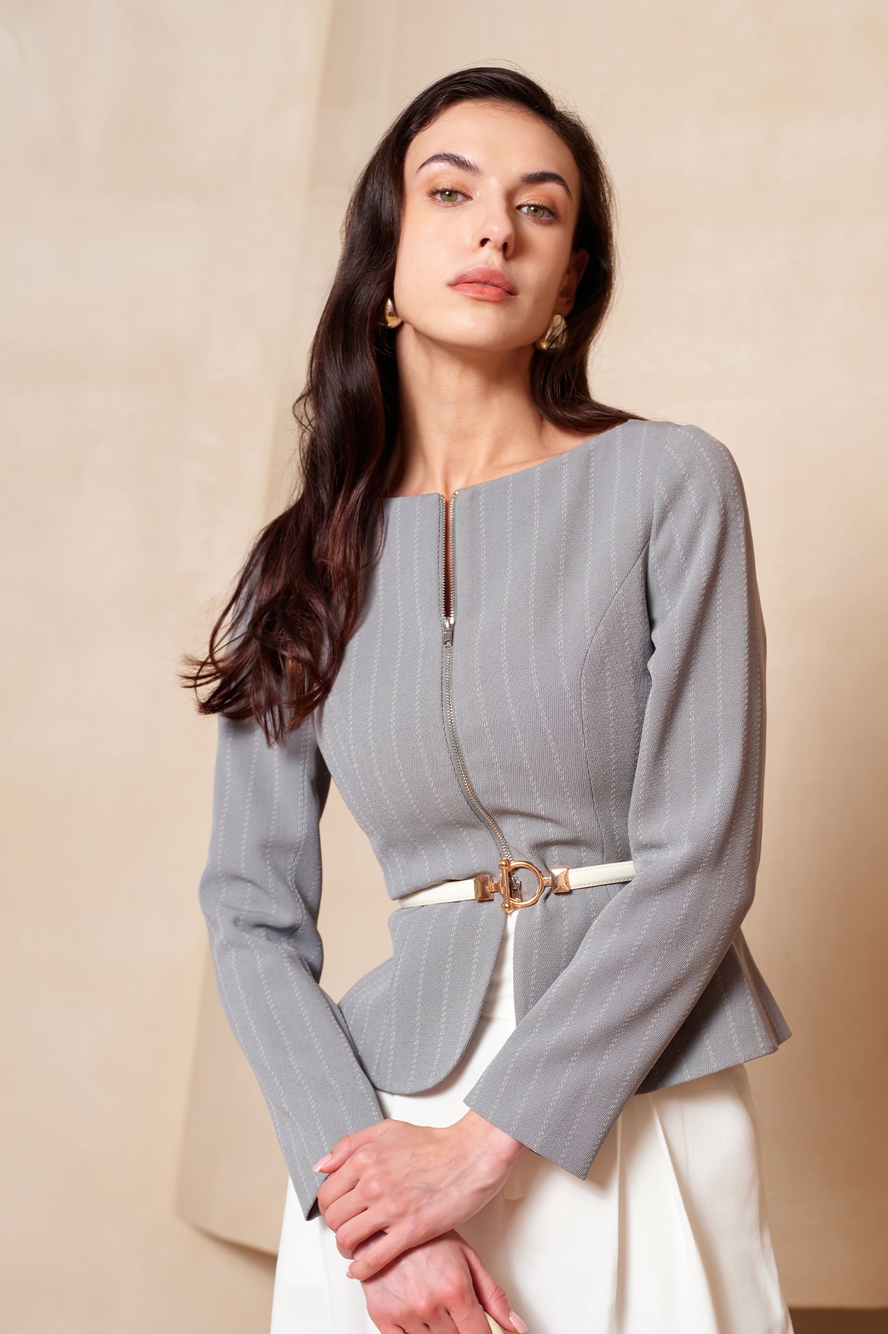 A professional woman wearing a sophisticated grey pinstripe zip-up blazer, featuring a thin white belt with a gold buckle and a tailored slim fit for a modern office look.