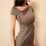 A professional woman wearing a sophisticated taupe grey sheath dress, featuring a chic asymmetric neckline, cap sleeves, and a tailored slim-fit silhouette for an elegant office look.