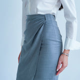 A professional woman wearing a sophisticated grey pencil skirt, featuring an elegant tulip hem and flattering side ruched detailing for a polished office look.
