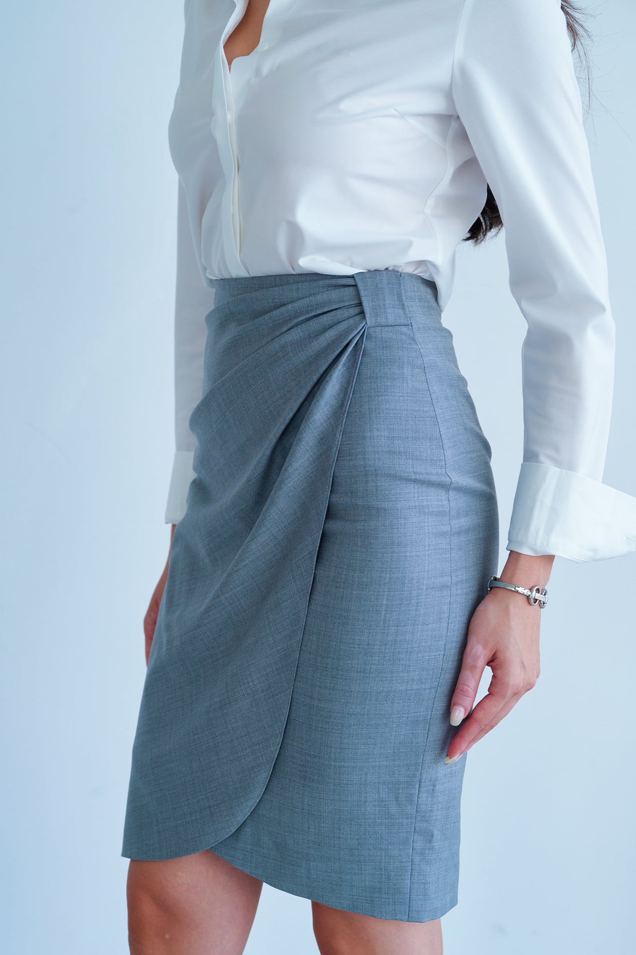 A professional woman wearing a sophisticated grey pencil skirt, featuring an elegant tulip hem and flattering side ruched detailing for a polished office look.