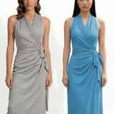 Two professional models wearing elegant halter-neck wrap maxi dresses in heather grey and vibrant sky blue, featuring a sophisticated draped V-neckline and waist tie for a minimalist summer or resort look.