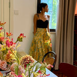 A professional woman wearing a sophisticated high-waisted A-line skirt, featuring a luxurious gold and teal wave pattern jacquard fabric and elegant full-skirt volume for a formal event.