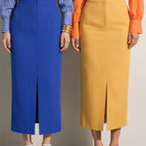 A style comparison of two elegant tailored midi pencil skirts with a sharp front slit; the left showcasing a vibrant royal blue high-waisted skirt paired with a striped shirt, and the right featuring a rich mustard yellow version paired with a bright orange blouse.