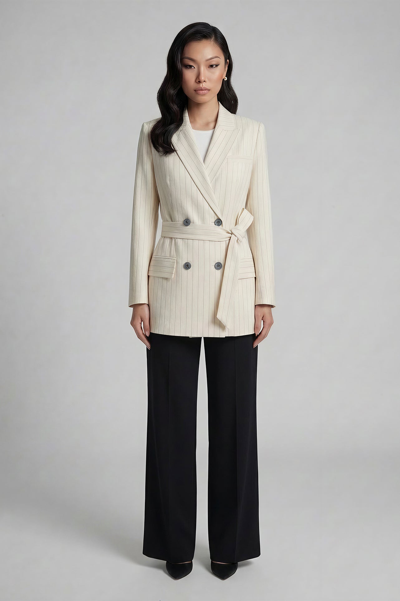 A professional woman wearing a sophisticated cream pinstripe blazer, featuring a double-breasted front with a chic waist-tie belt and notched lapels for a polished old money office look.