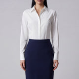 A professional woman wearing a classic crisp white long-sleeve slim-fit blouse with a sharp point collar, styled with a navy blue pencil skirt for a polished executive office look.