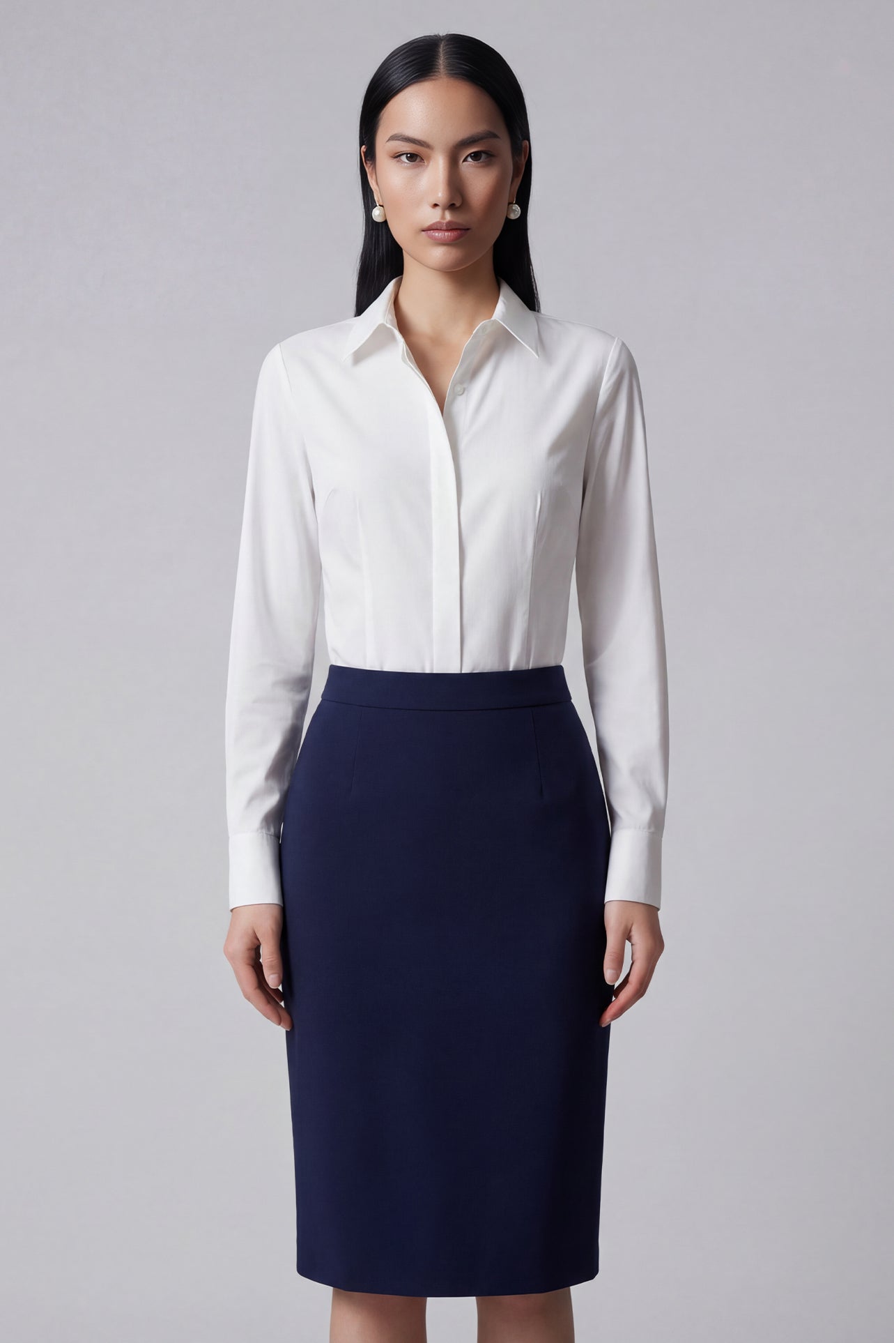 A professional woman wearing a classic crisp white long-sleeve slim-fit blouse with a sharp point collar, styled with a navy blue pencil skirt for a polished executive office look.