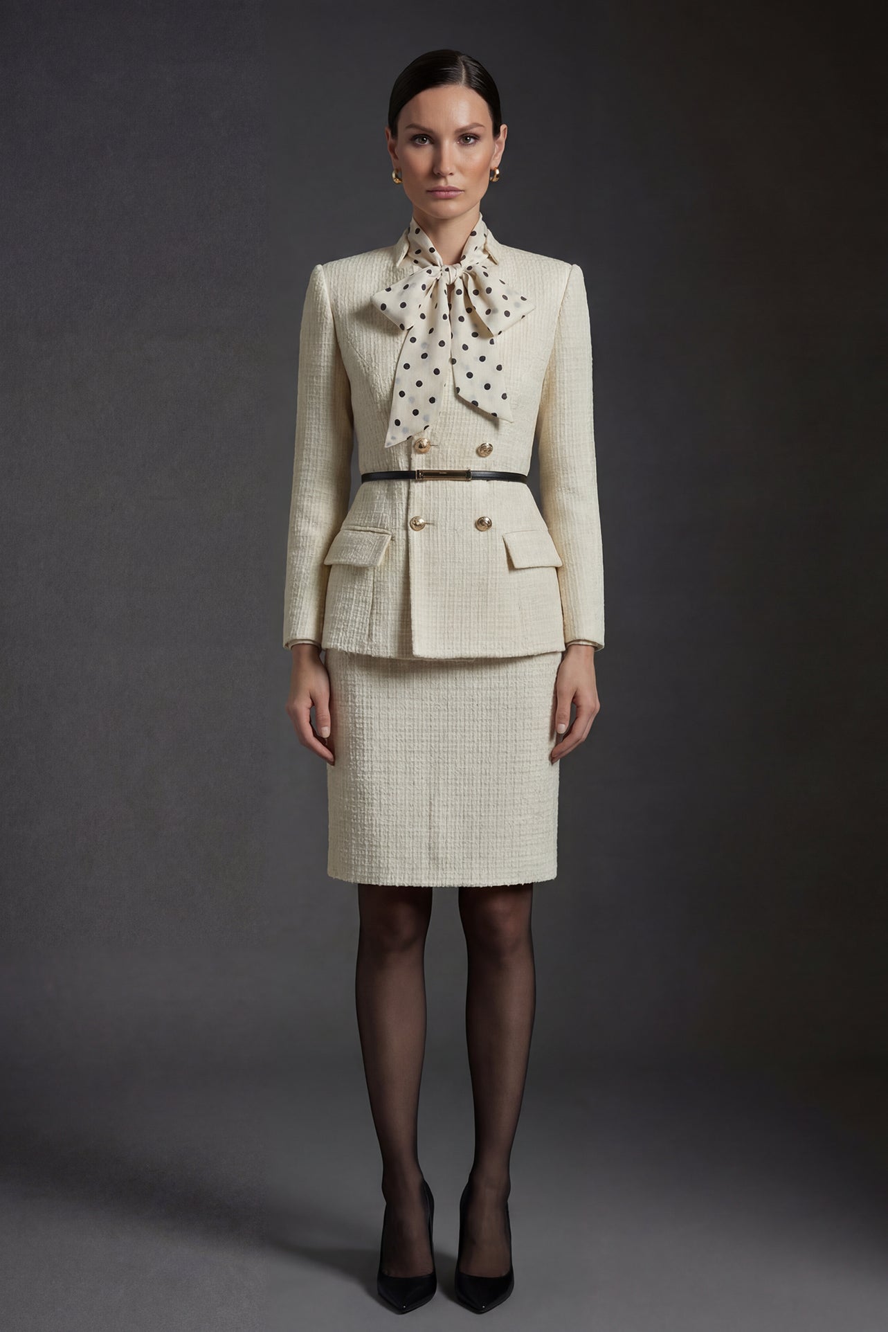 A professional woman wearing a sophisticated cream white tweed skirt suit, featuring a double-breasted blazer with gold buttons, a slim black belt, and an elegant polka dot pussy bow tie for a polished French chic office look.
