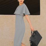 A stylish woman walking on a city street wearing an elegant light grey sheath midi dress with a sophisticated capelet sleeve design, round neckline, and side slit, carrying a black leather handbag.
