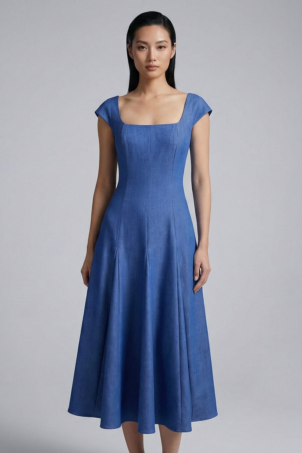 A professional woman modeling an elegant mid-blue midi dress featuring a structured square neckline, delicate cap sleeves, and a flattering high-waisted A-line flare skirt for a sophisticated summer look.