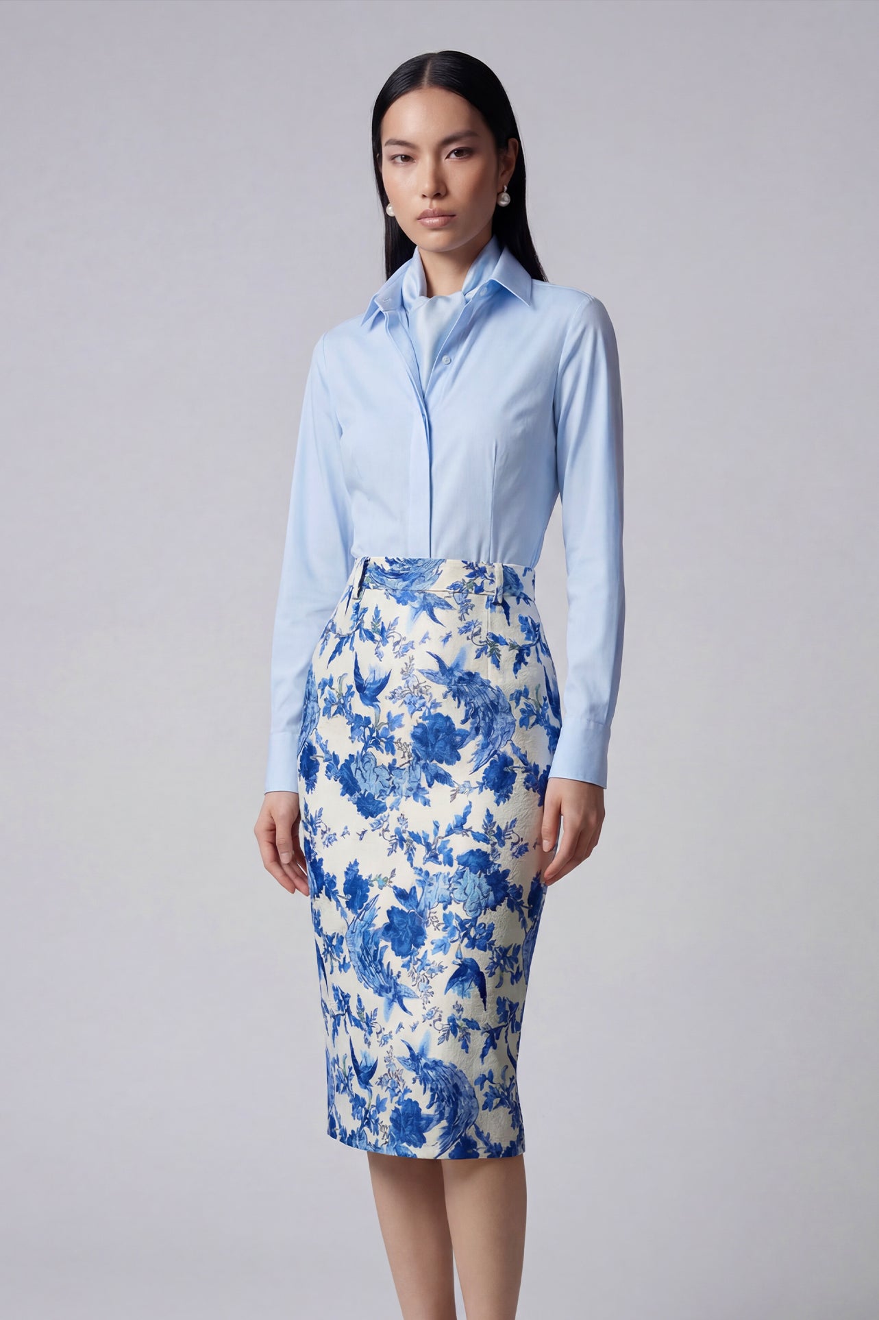 An elegant professional woman wearing a high-waisted pencil skirt featuring a sophisticated blue and white floral porcelain-style print, perfect for a polished office look.