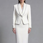 Two elegant professional women modeling high-end monochrome executive suits, one in a black blazer with white piping and wide-leg trousers, the other in a white blazer with dark trim and a matching pencil skirt.