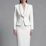 Two elegant professional women modeling high-end monochrome executive suits, one in a black blazer with white piping and wide-leg trousers, the other in a white blazer with dark trim and a matching pencil skirt.