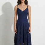 A professional woman modeling an elegant navy blue lace midi dress, featuring delicate V-neck spaghetti straps, a tailored fit-and-flare silhouette, and a beautiful flowing asymmetric handkerchief lace trim hem.
