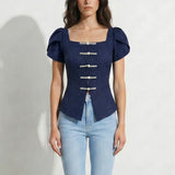 A professional woman modeling an elegant navy blue lace short top, featuring a retro square neckline, romantic short puff sleeves, and a series of pearl and rhinestone frog closures on the front with a tailored triangular split hem, paired with light blue high-waisted jeans.
