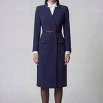 An elegant professional woman wearing a sophisticated navy blue double-breasted long coat dress, featuring a black waist belt and structured shoulders for a powerful executive look.