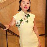 A professional woman wearing a stunning pale yellow sleeveless dress, featuring a traditional mandarin collar, exquisite white floral embroidery appliques along the neckline and hem, and an elegant side slit for a sophisticated modern oriental look.