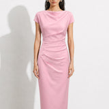 A professional woman modeling an elegant pastel pink satin midi dress, featuring a sophisticated cowl neckline, delicate cap sleeves, and slimming asymmetric ruched drapes across the waist for a quiet luxury look.