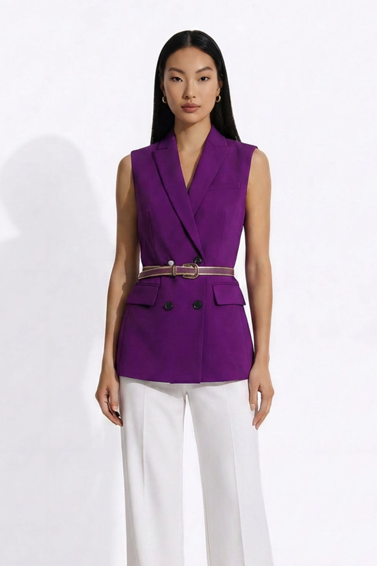 A professional woman modeling an elegant deep purple sleeveless double-breasted blazer vest, featuring a notched lapel, front flap pockets, and a slim belt, paired with white tailored trousers for a sophisticated office look.