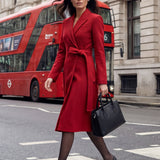 A sophisticated woman walking in London wearing an elegant vibrant red wrap coat dress, featuring a tie-waist belt and notched lapels for a polished executive street style look.