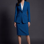 A professional woman wearing a sophisticated royal blue tailored skirt suit, featuring a slim-fit single-button blazer with structured shoulders and a matching midi pencil skirt for a powerful executive office look.