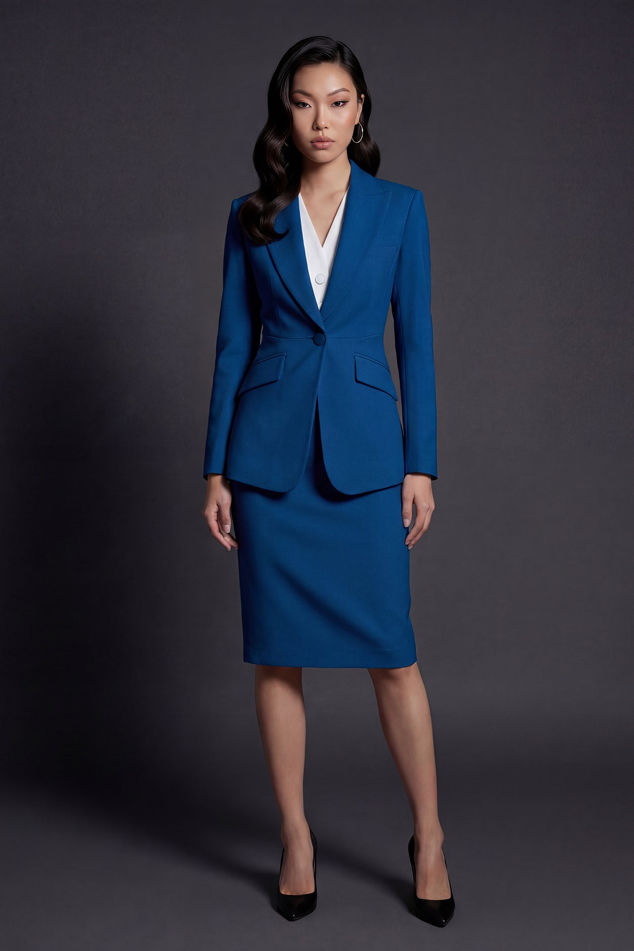 A professional woman wearing a sophisticated royal blue tailored skirt suit, featuring a slim-fit single-button blazer with structured shoulders and a matching midi pencil skirt for a powerful executive office look.