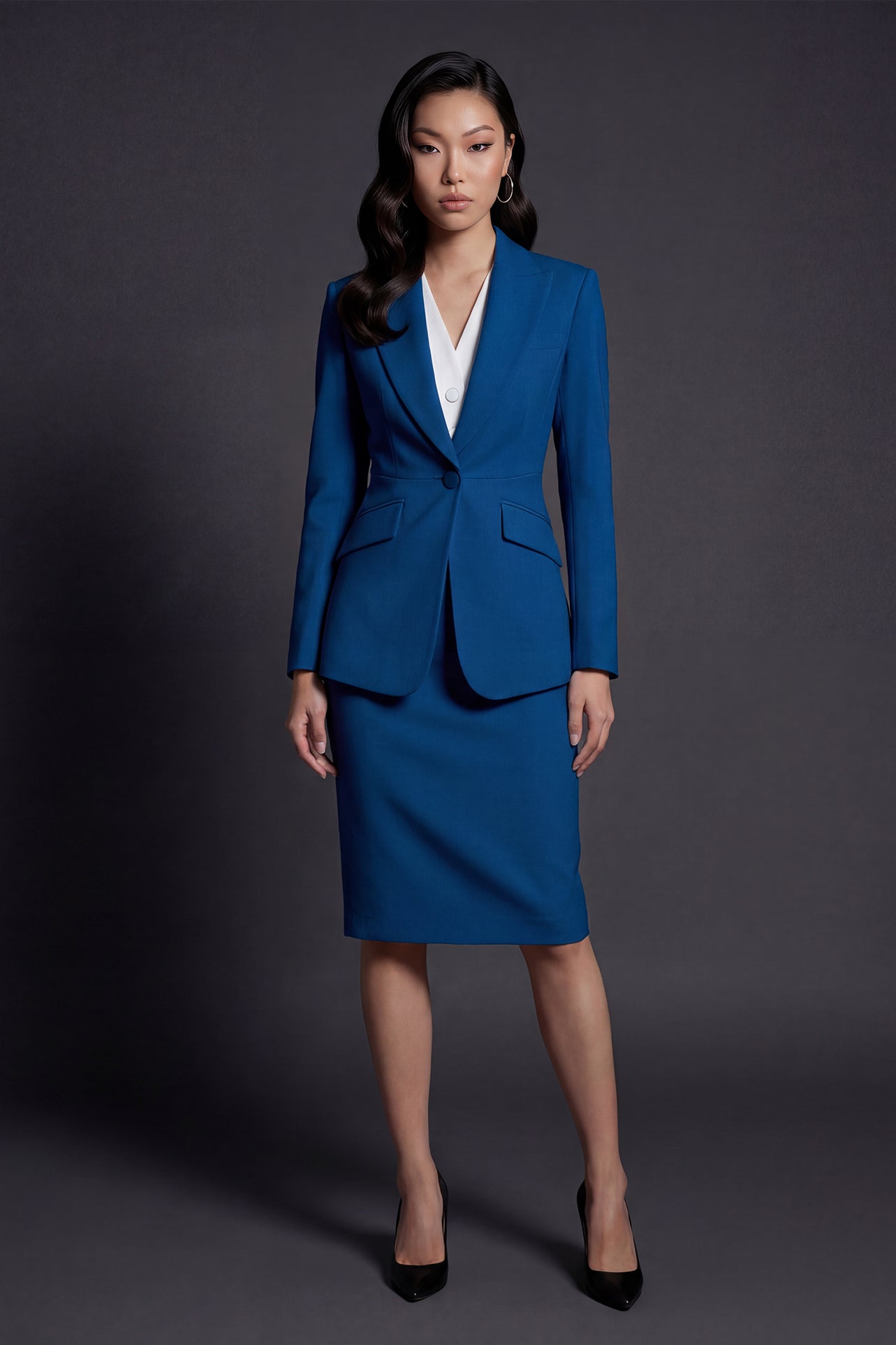 A professional woman wearing a sophisticated royal blue tailored skirt suit, featuring a slim-fit single-button blazer with structured shoulders and a matching midi pencil skirt for a powerful executive office look.