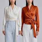 A professional woman wearing a high-end white silk wrap blouse with a side-tie detail, paired with a tailored black high-waisted pencil skirt for a sophisticated executive office look.