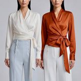 A professional woman wearing a high-end white silk wrap blouse with a side-tie detail, paired with a tailored black high-waisted pencil skirt for a sophisticated executive office look.