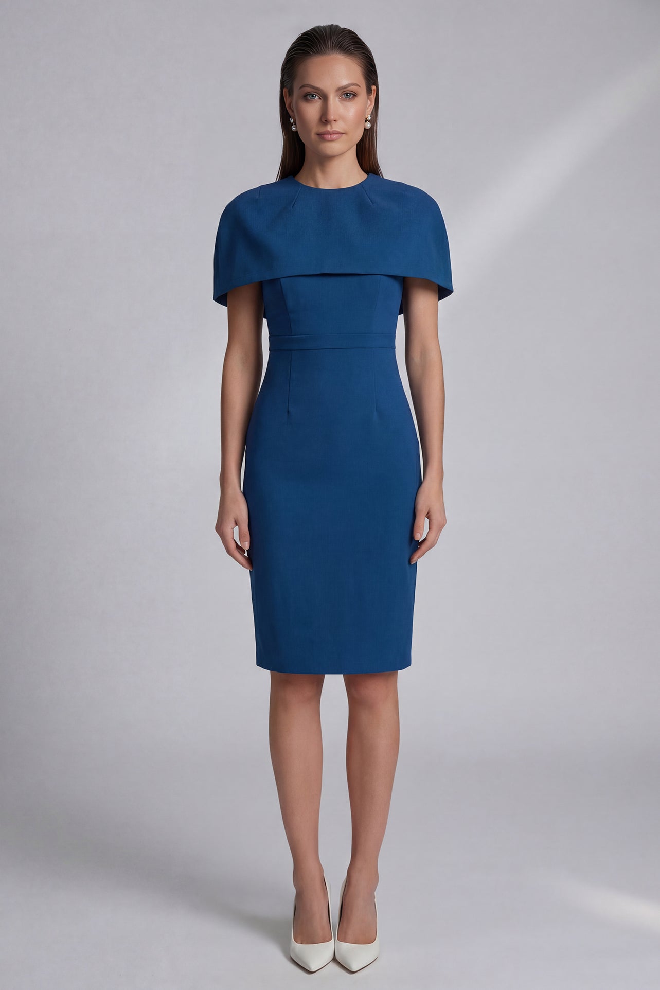 A professional woman wearing a sophisticated teal blue midi dress with an elegant cape-style overlay and structured shoulders, perfect for formal executive events and ceremonial occasions.