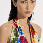 A close-up view of a professional model showcasing an elegant multi-color tropical floral print halter dress, featuring a sophisticated plunge V-neckline and vibrant red, blue, and yellow blossom patterns for a chic summer resort look.