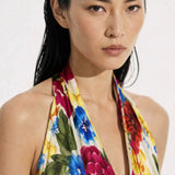 A close-up view of a professional model showcasing an elegant multi-color tropical floral print halter dress, featuring a sophisticated plunge V-neckline and vibrant red, blue, and yellow blossom patterns for a chic summer resort look.