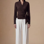 Two models presenting versatile textured wrap tops in cream and dark chocolate, featuring a slimming V-neck and elegant side-tie waist, styled with a tan pencil skirt and white high-waisted trousers.