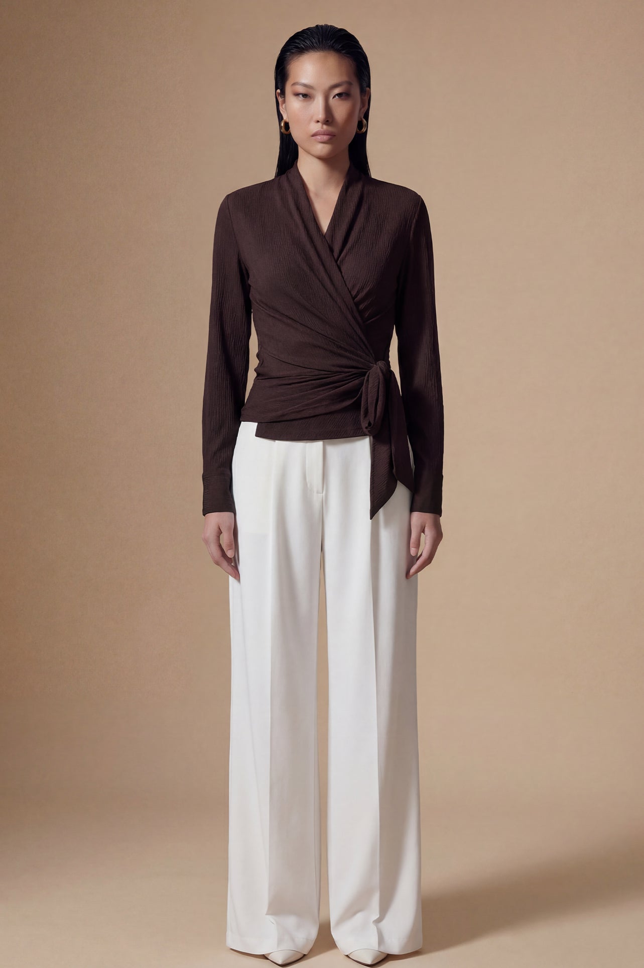 Two models presenting versatile textured wrap tops in cream and dark chocolate, featuring a slimming V-neck and elegant side-tie waist, styled with a tan pencil skirt and white high-waisted trousers.