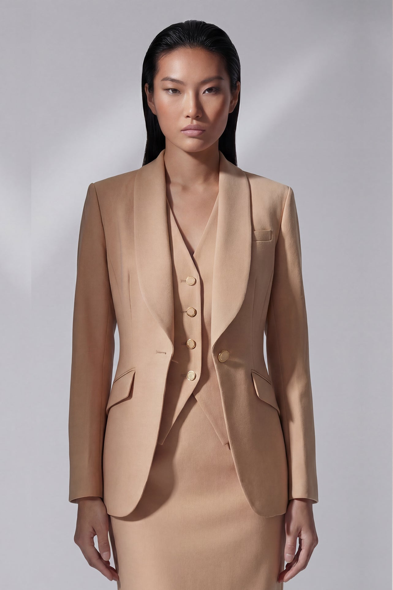 Two professional women showcasing high-end executive business suits: one in a crisp white pant suit with a shawl lapel blazers, and the other in a sophisticated camel skirt suit with a tailored vest, perfect for formal corporate settings.
