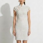 A professional woman modeling an elegant white lace modern qipao dress, featuring an intricate eyelet textured fabric, a sophisticated mandarin collar with a traditional knot button, and slimming cap sleeves.