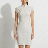 A professional woman modeling an elegant white lace modern qipao dress, featuring an intricate eyelet textured fabric, a sophisticated mandarin collar with a traditional knot button, and slimming cap sleeves.