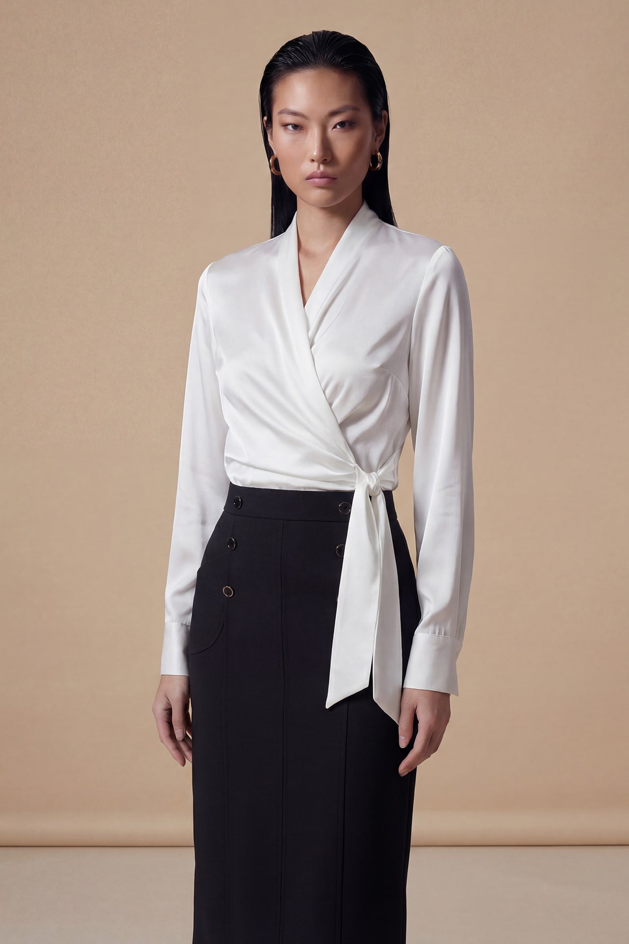 A professional woman wearing a high-end white silk wrap blouse with a side-tie detail, paired with a tailored black high-waisted pencil skirt for a sophisticated executive office look.