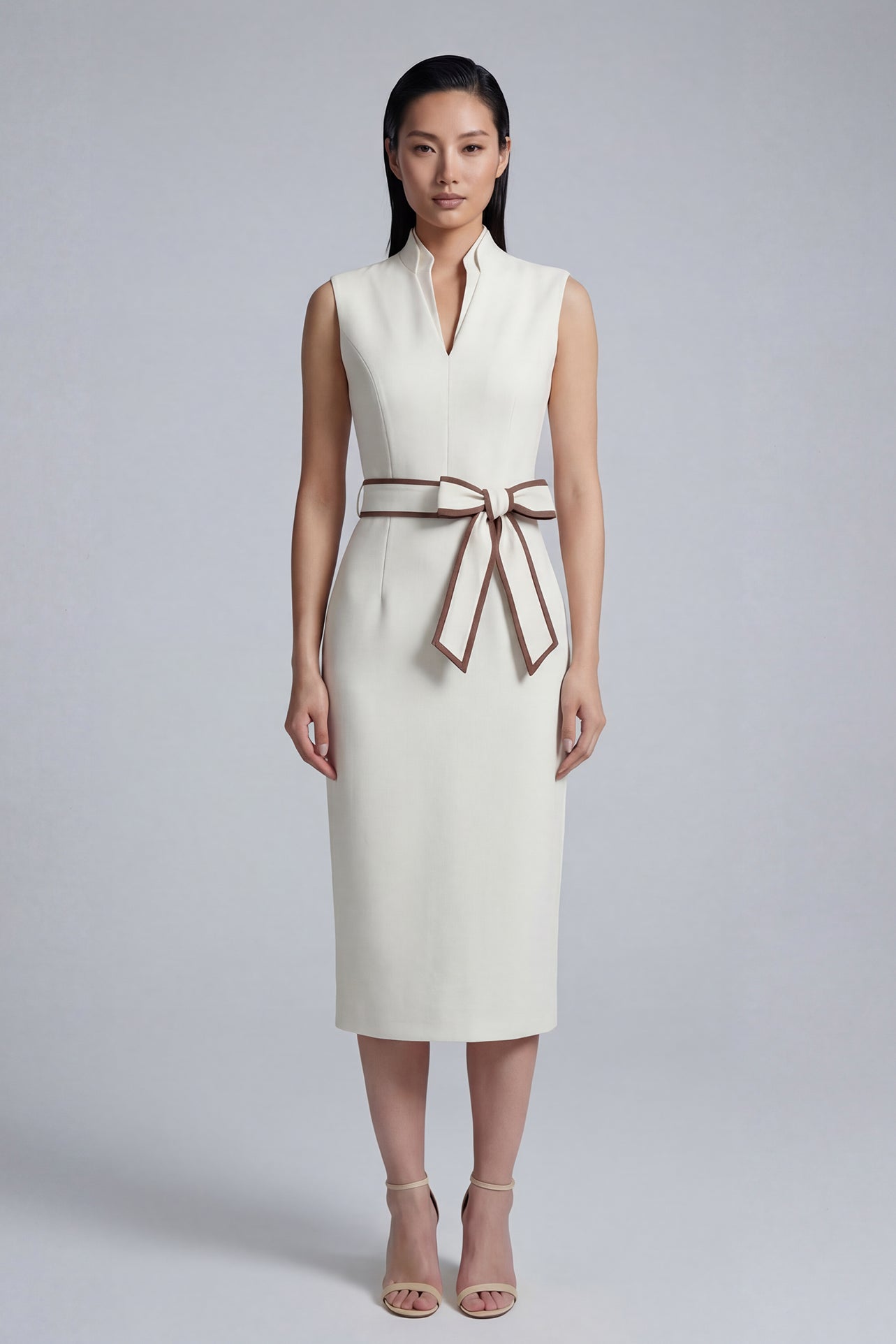 A professional woman modeling an elegant white sleeveless midi dress, featuring a sophisticated stand collar with a V-neck slit and a chic brown contrast bow belt for a polished office look.